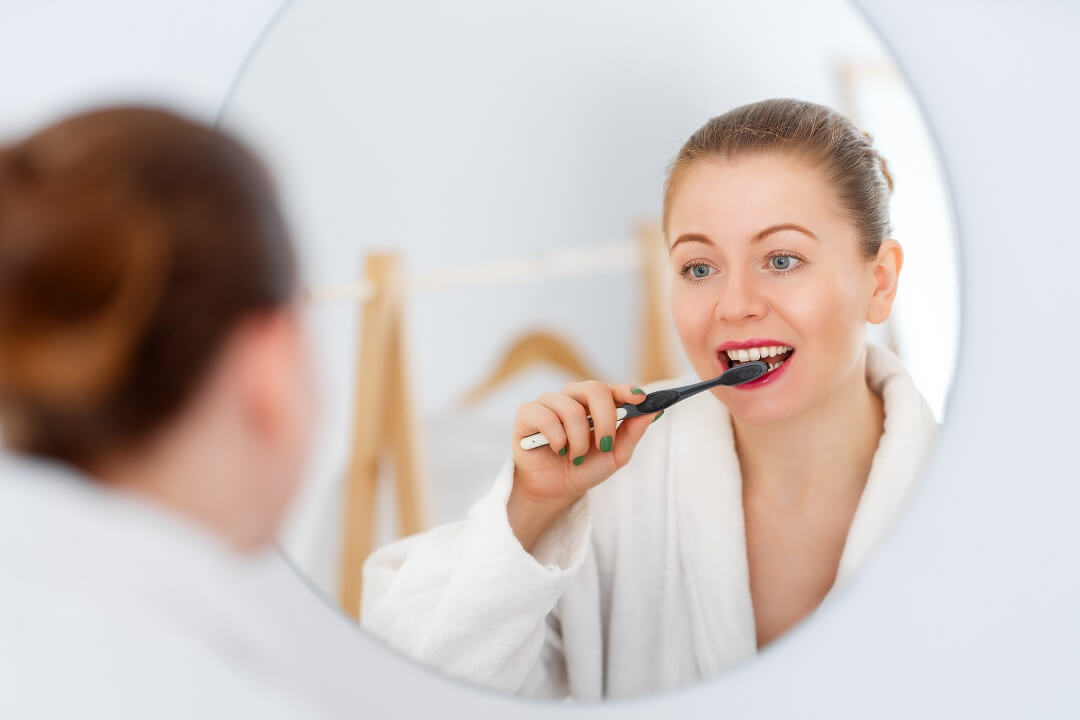 Woman wearing white bathrobe brushing her teeth in front of the mirror