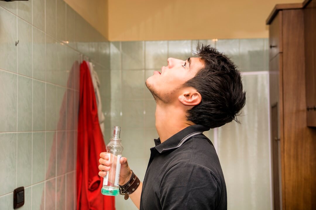 Young man using mouthwash in bathroom