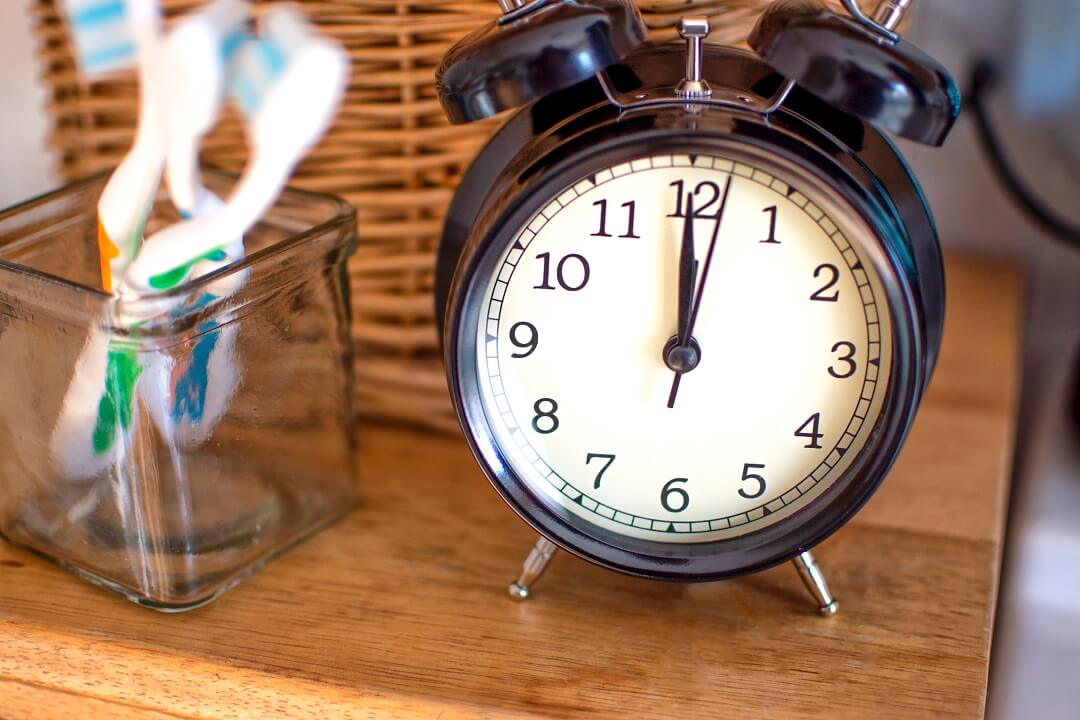 A set of toothbrush in a glass and a table clock